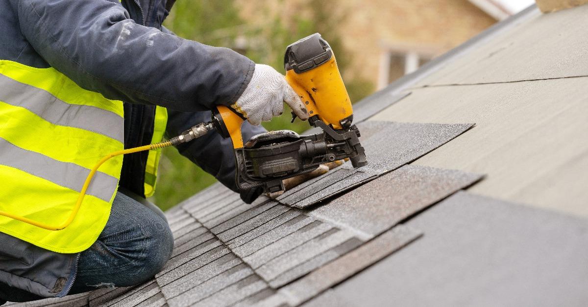 Workman using pneumatic nail gun install tile on roof of new house under construction