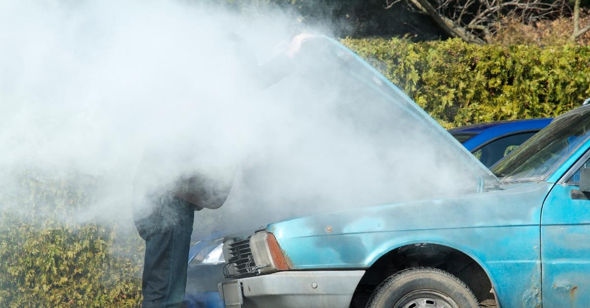 man looking at a smoking engine in his car