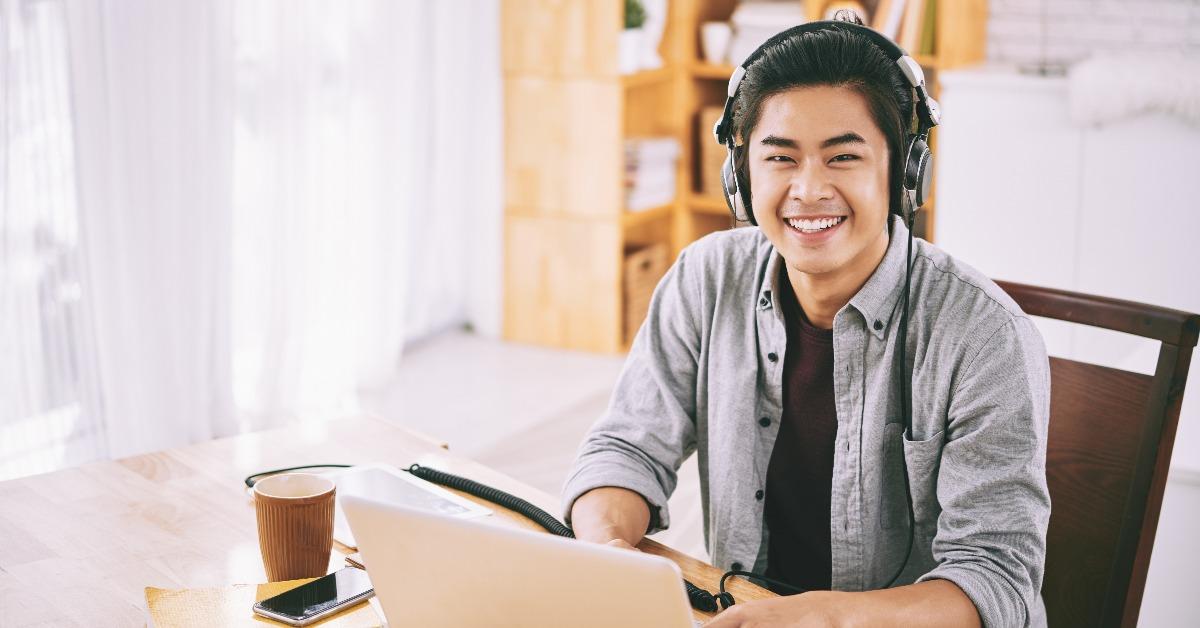 asian student in headphones working on laptop at home