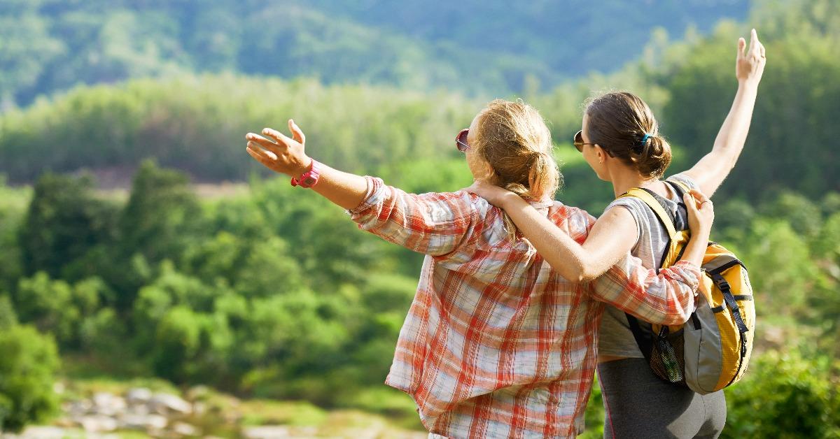 two smiling young women with backpacks looking at on mountains