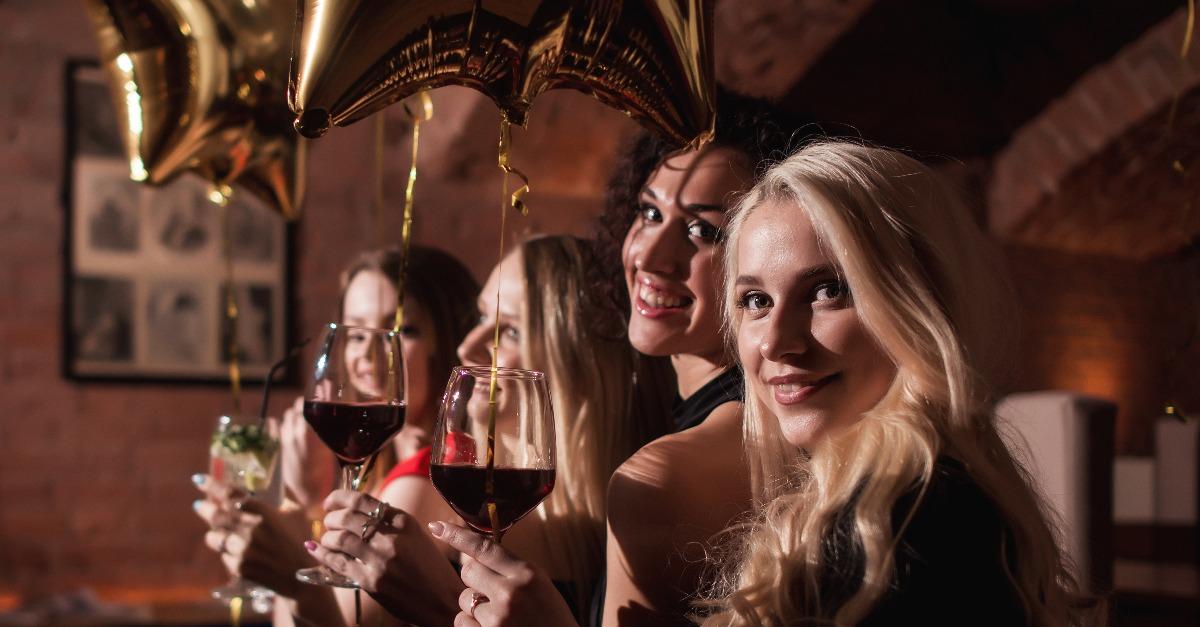 cheerful young women standing looking back to camera holding glasses of wine