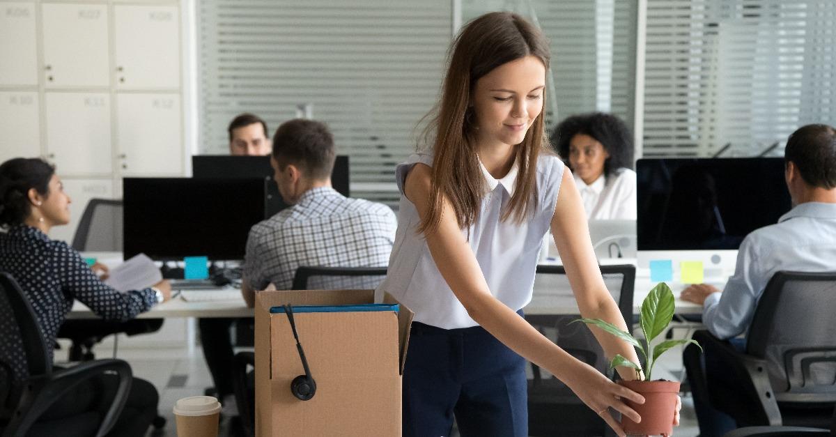 smiling hired female company employee unpacking box with personal belongings at workplace