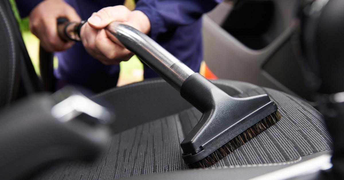 man hoovering seat of car during car cleaning