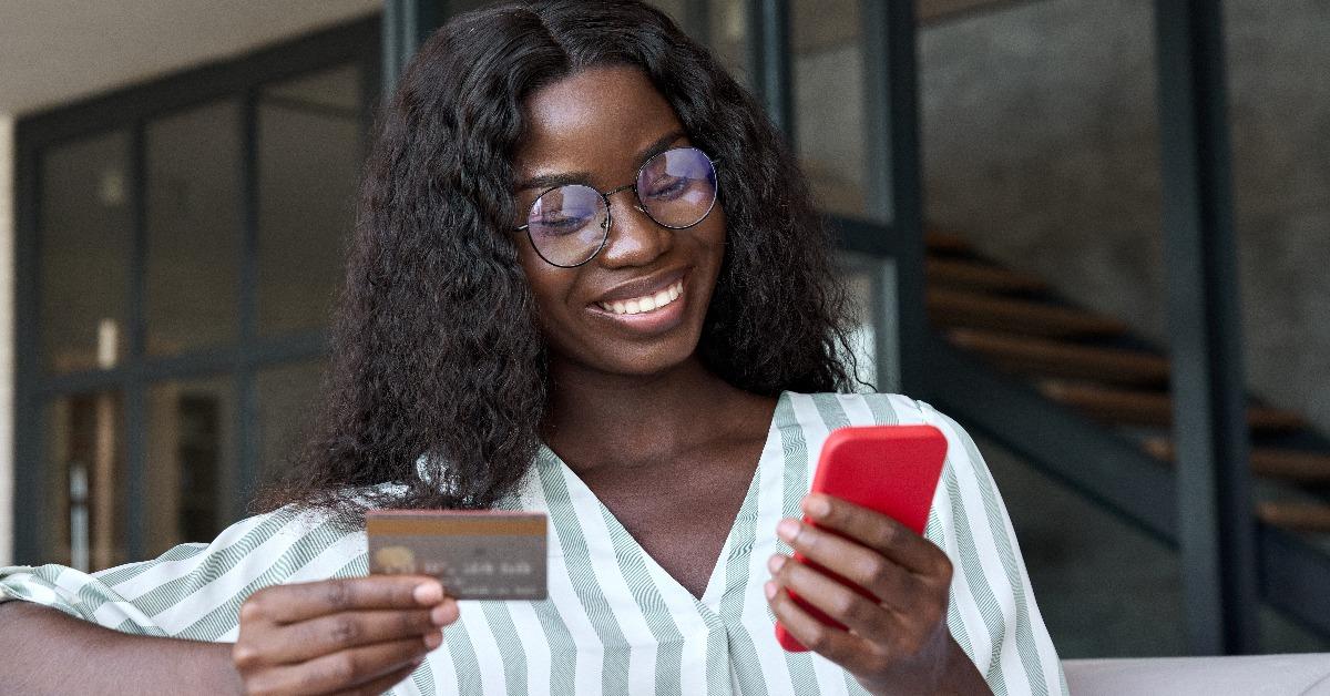 african woman shopper holding credit card using cell phone mobile app