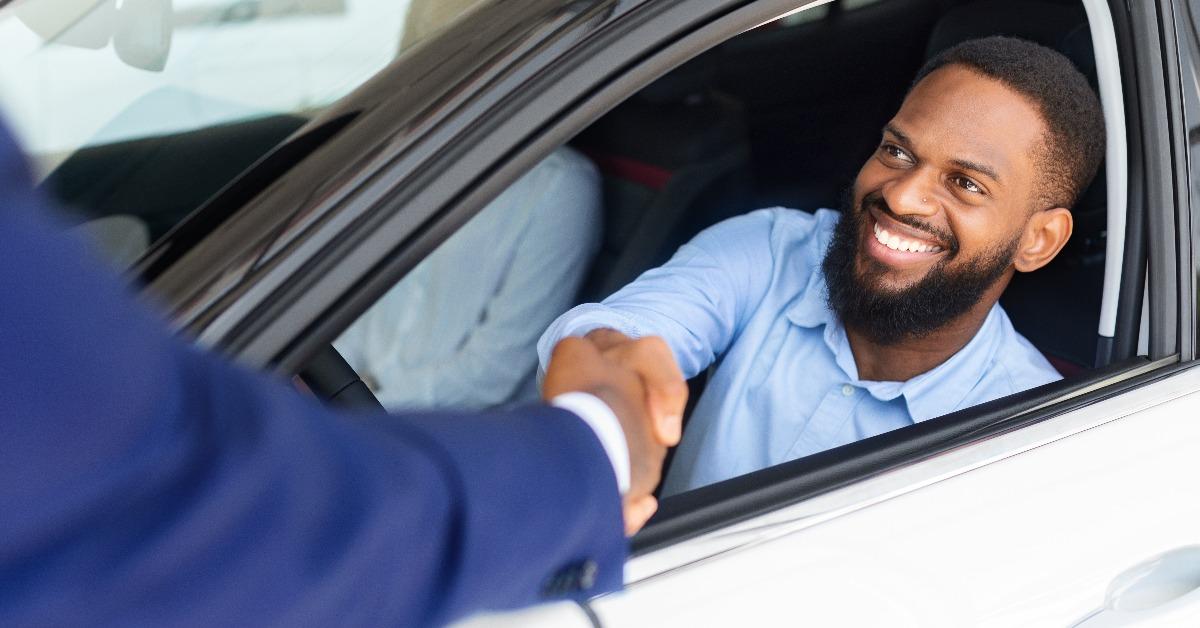 black man sitting inside of new car and shaking hands with salesman