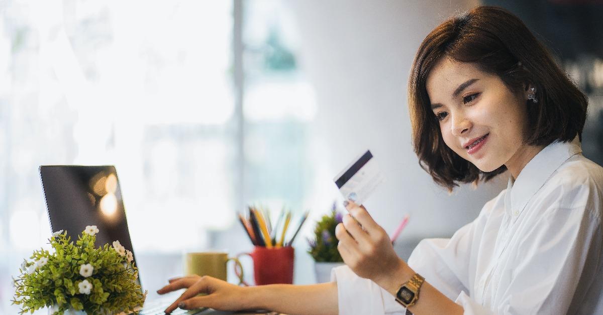 young woman holding credit card and using laptop computer