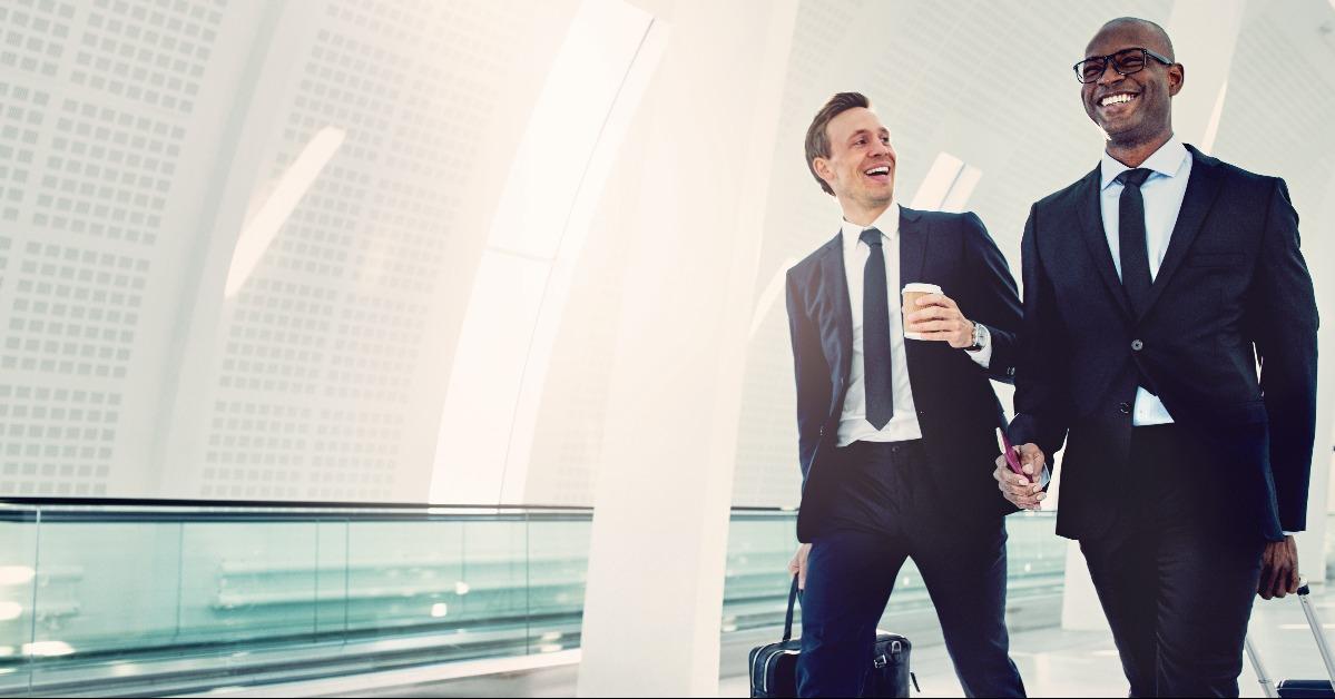 smiling businessmen walking through an airport talking together