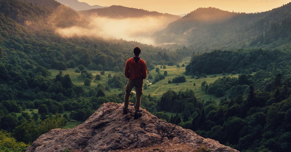 man standing on top of cliff at sunset
