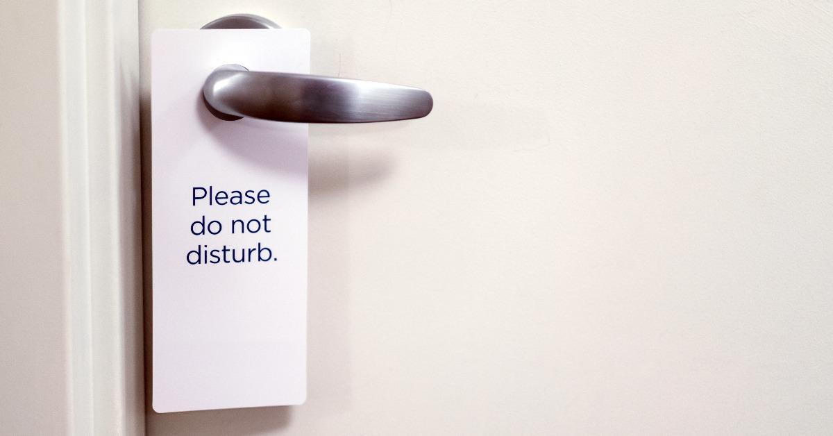 closed white door of hotel room with please do not disturb sign