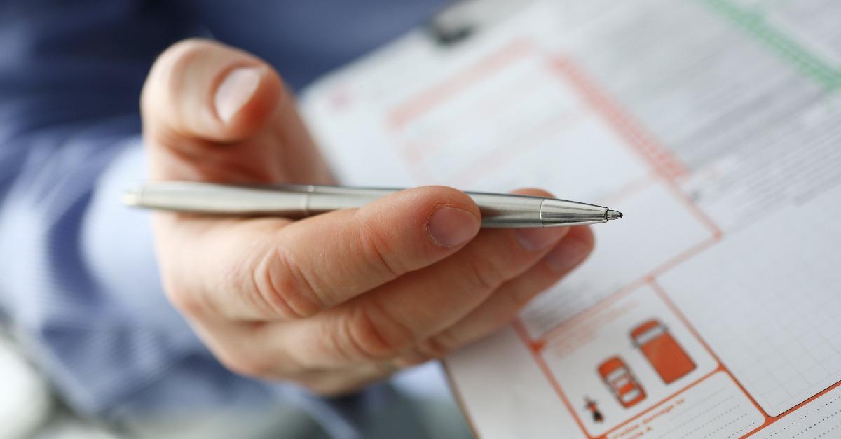 male insurer hand hold silver pen over an accident form