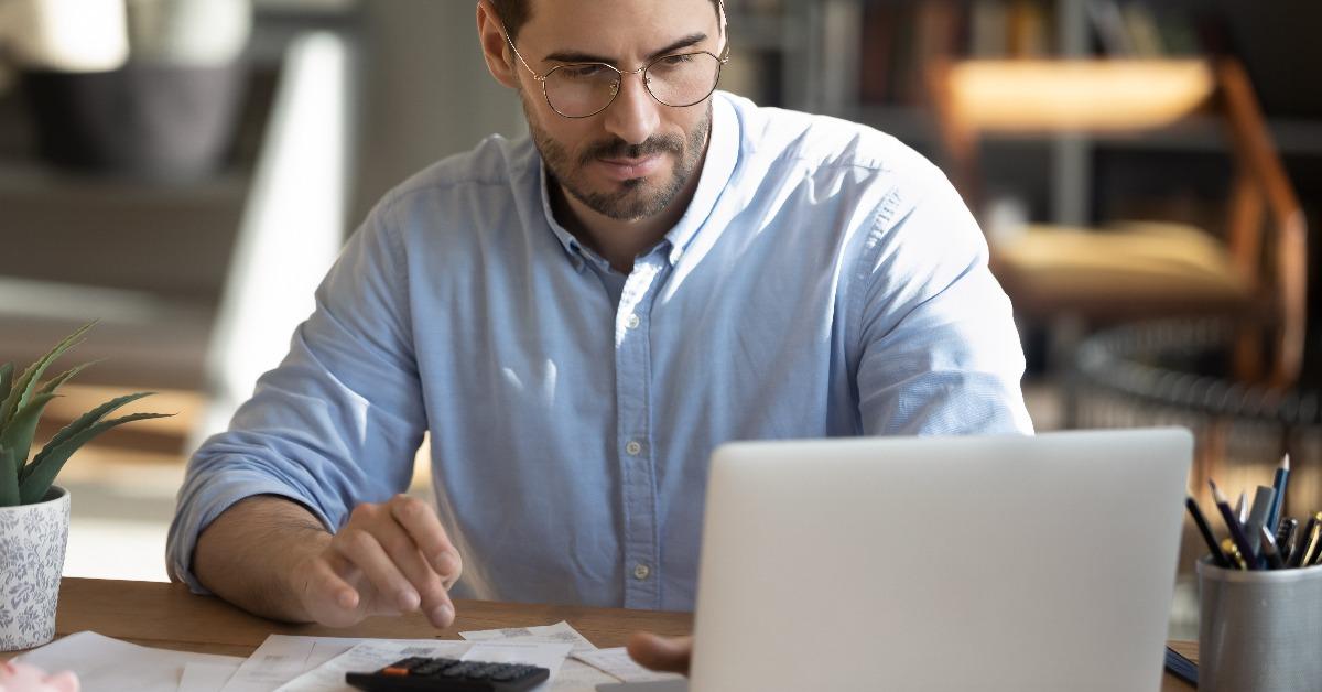 young man looking at laptop screen calculating expenses 