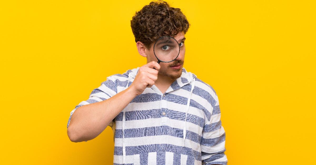 blonde man over yellow wall taking a magnifying glass