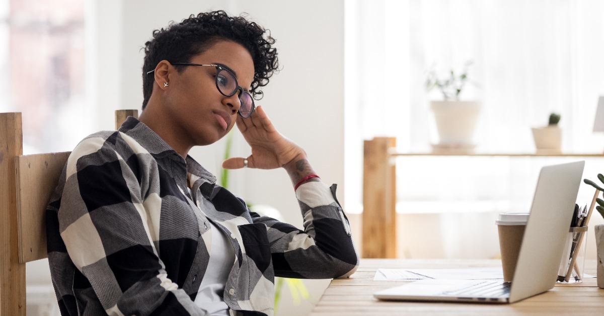African American girl bored at workplace looking at laptop screen