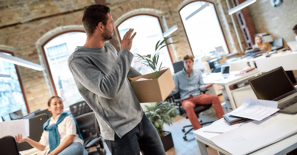 man in casual wear holding box with personal things and saying good bye to his ex-colleagues