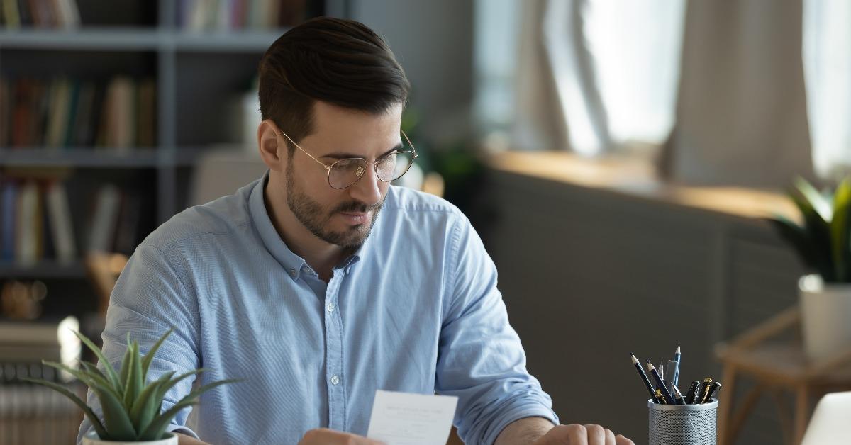 Serious man wearing glasses checking bills using calculator