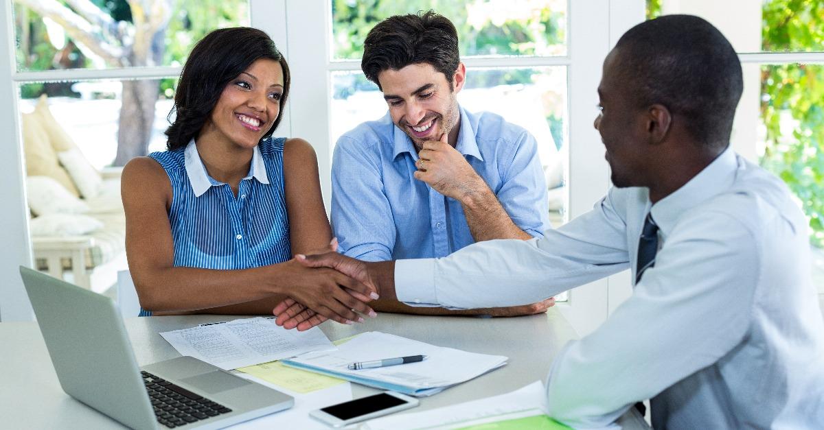 Happy mixed race couple shaking hands with real estate agent