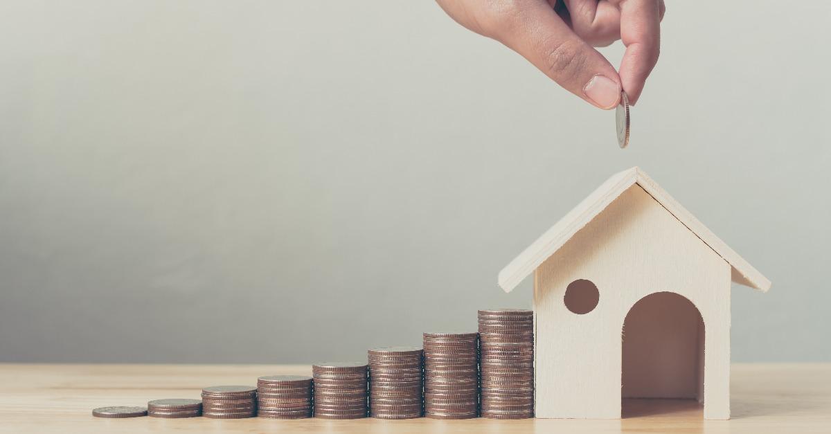 Hand putting money coin stack to the wooden house