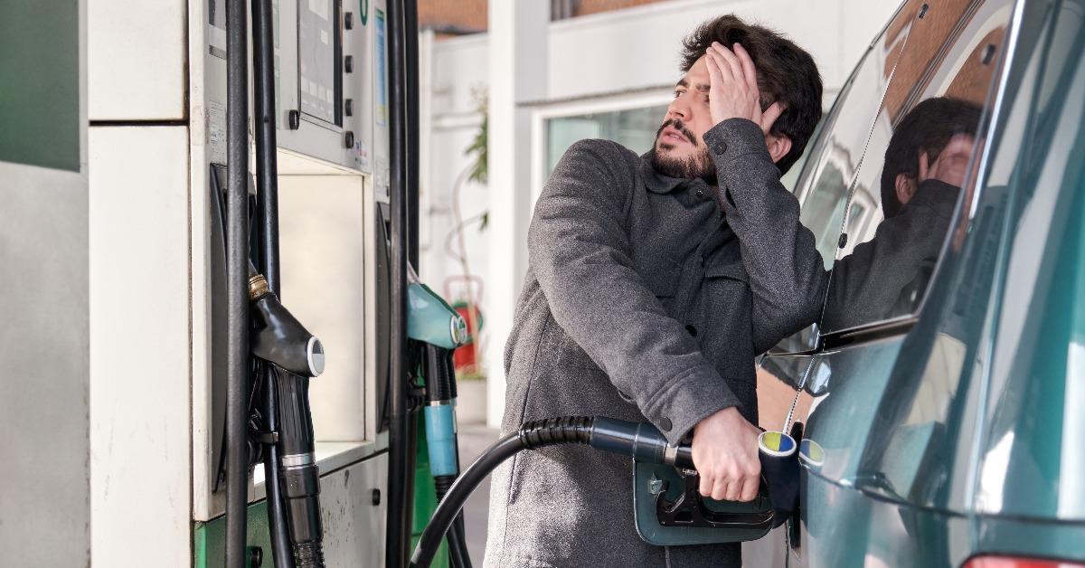 Young man refueling his vehicle while looking worried at the high gas prices