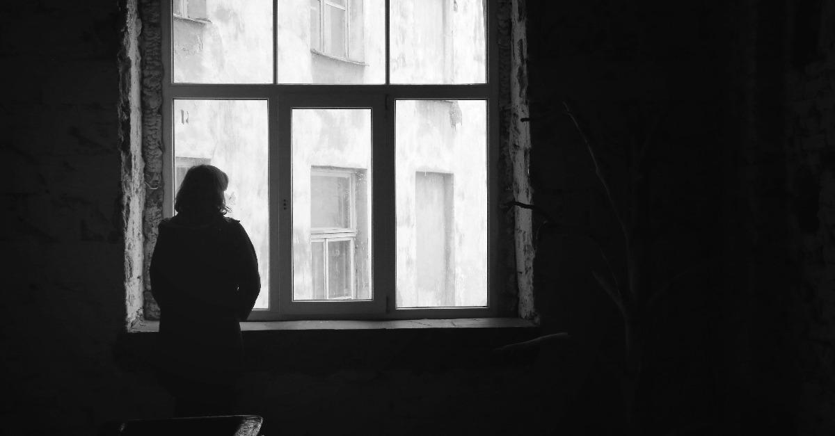 woman looking out of the window in dark deserted house