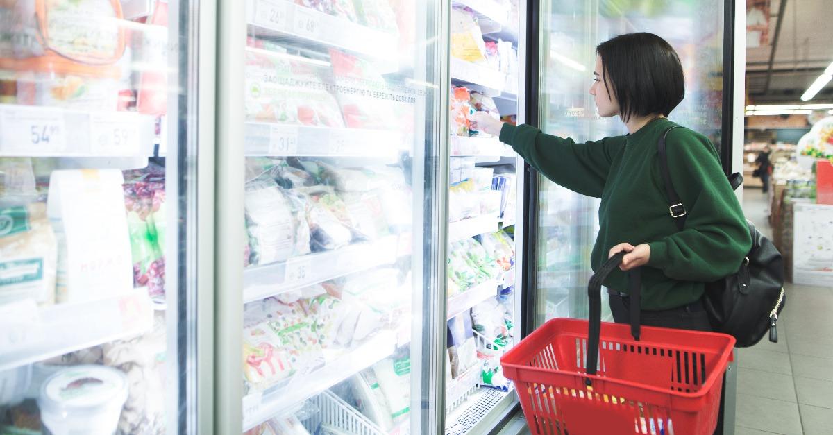 A girl with a basket takes frozen foods from the supermarket's refrigerator