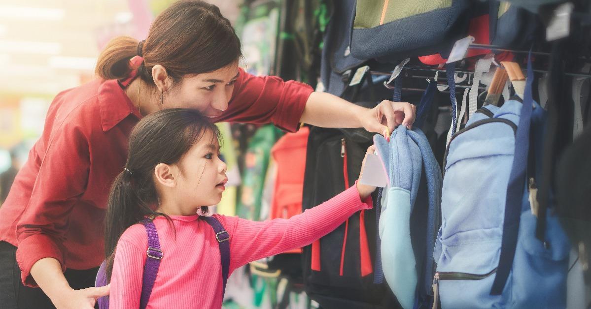 mother and daughter buying school satchel or bag in store