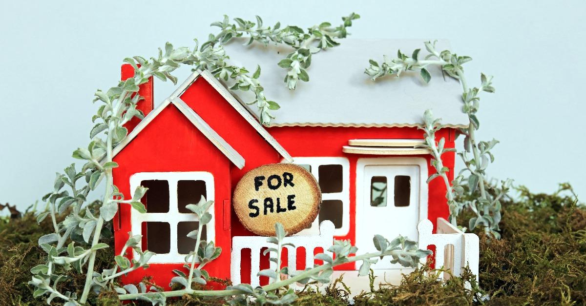 for sale sign written on a wooden log outside a run down scale model cottage