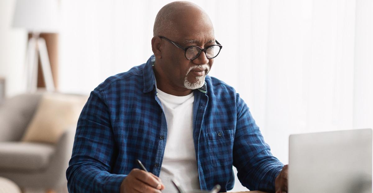 black man using laptop taking notes in office 