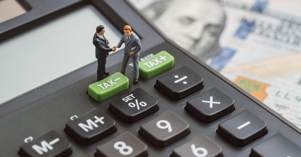 miniature people businessmen handshaking standing on TAX minus button on calculator 