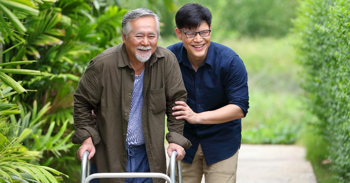 senior man using walker while walking for exercise around the garden with his son