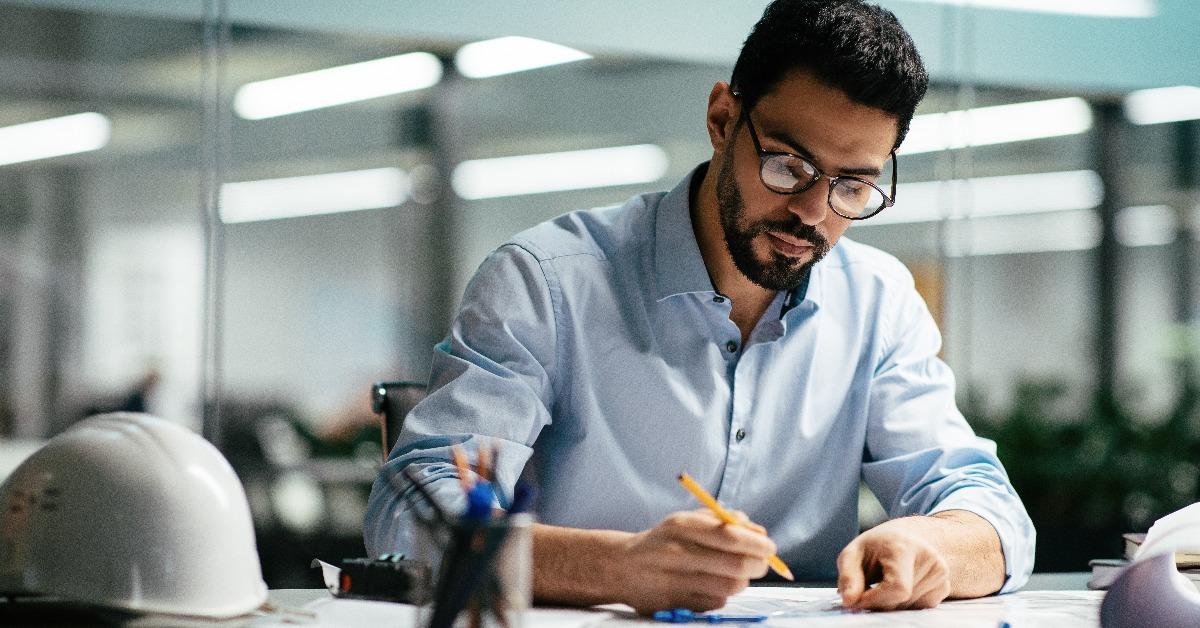 engineer in glasses with beard works with drawings at workplace