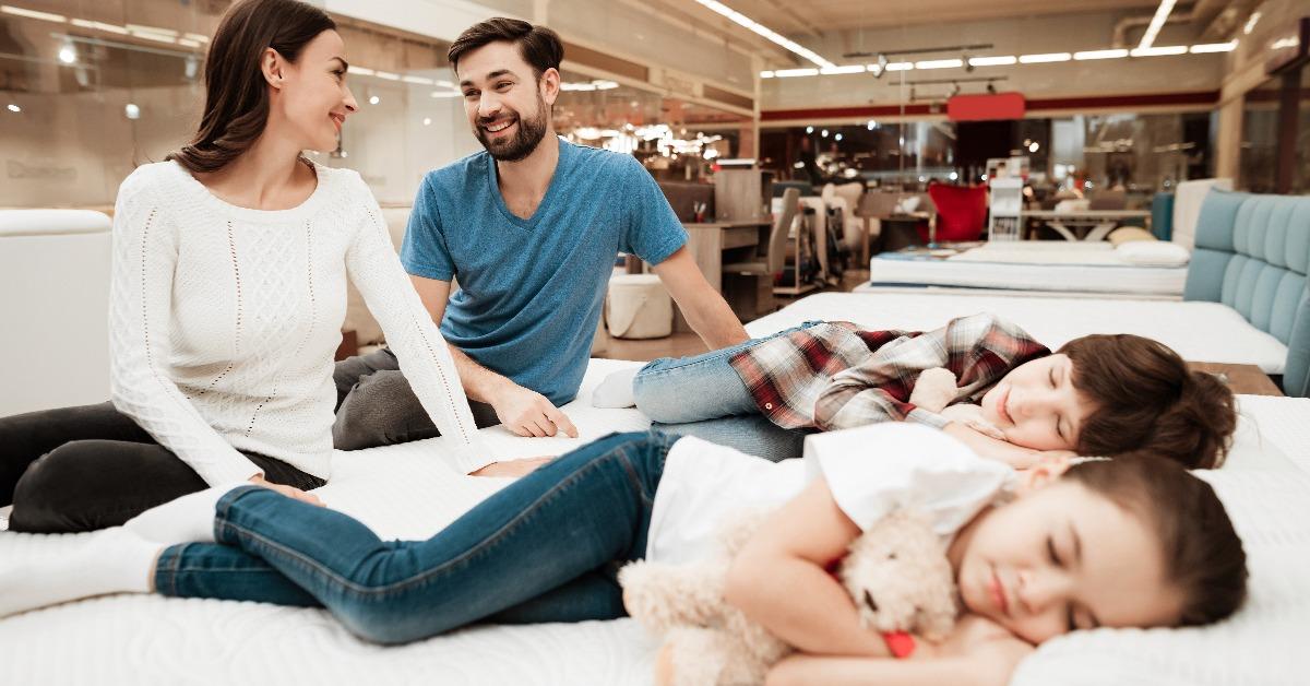 lovely couple is sitting on mattress next to sleeping children in furniture store