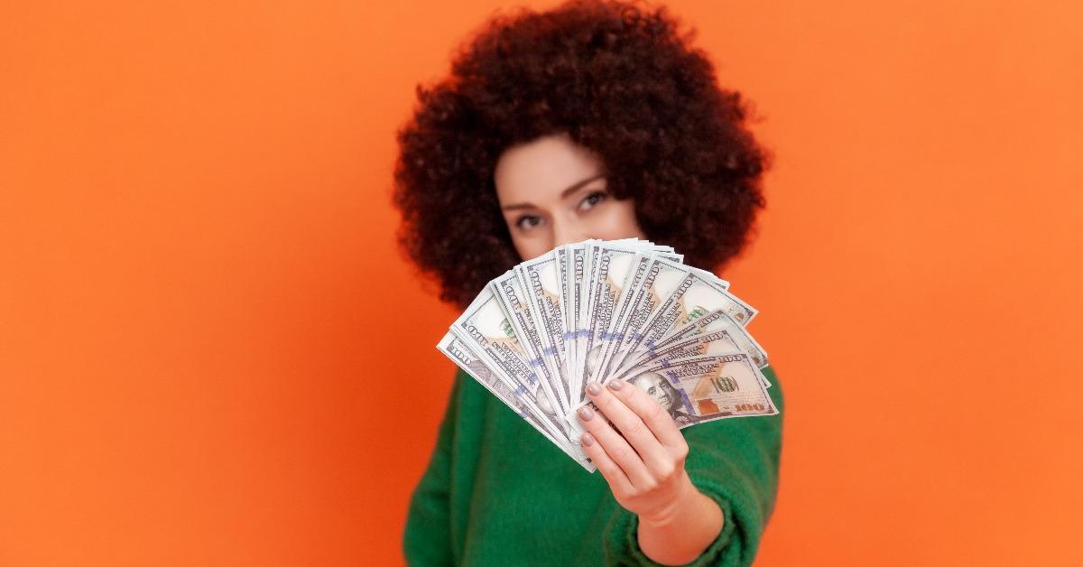 woman with Afro hairstyle holding out fan of dollars bills