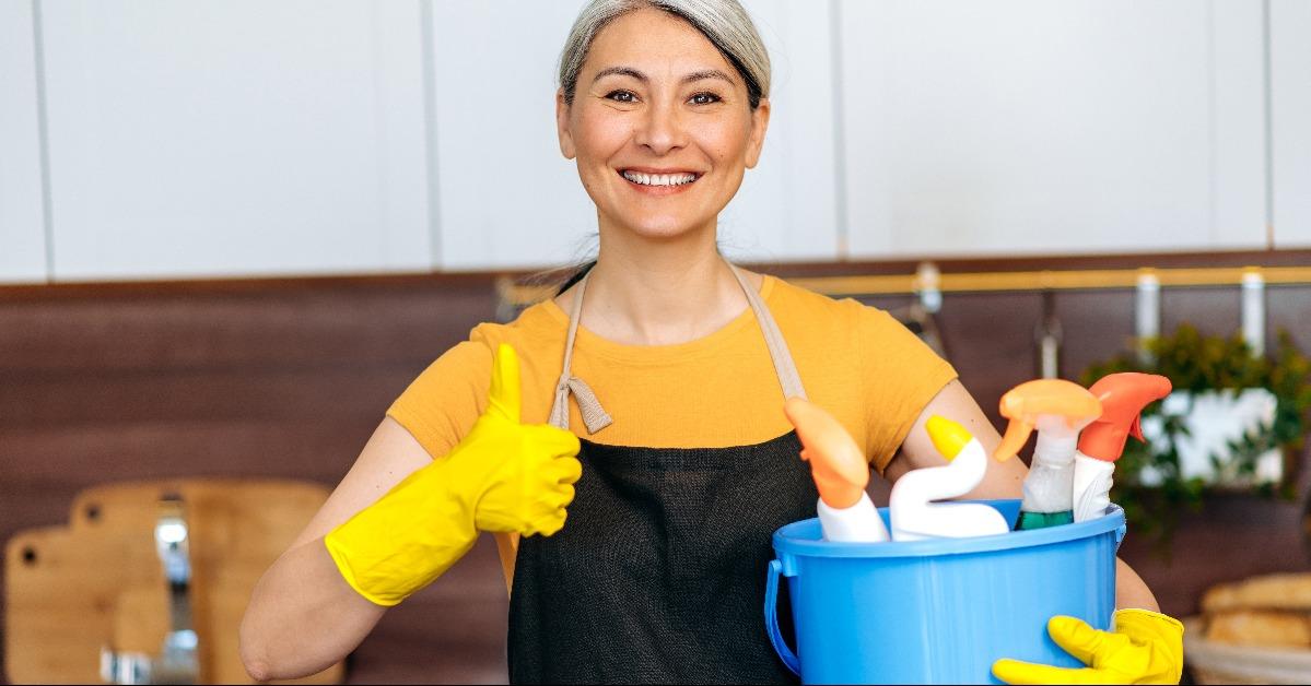 gray-haired woman is holding a bucket with detergents and rags