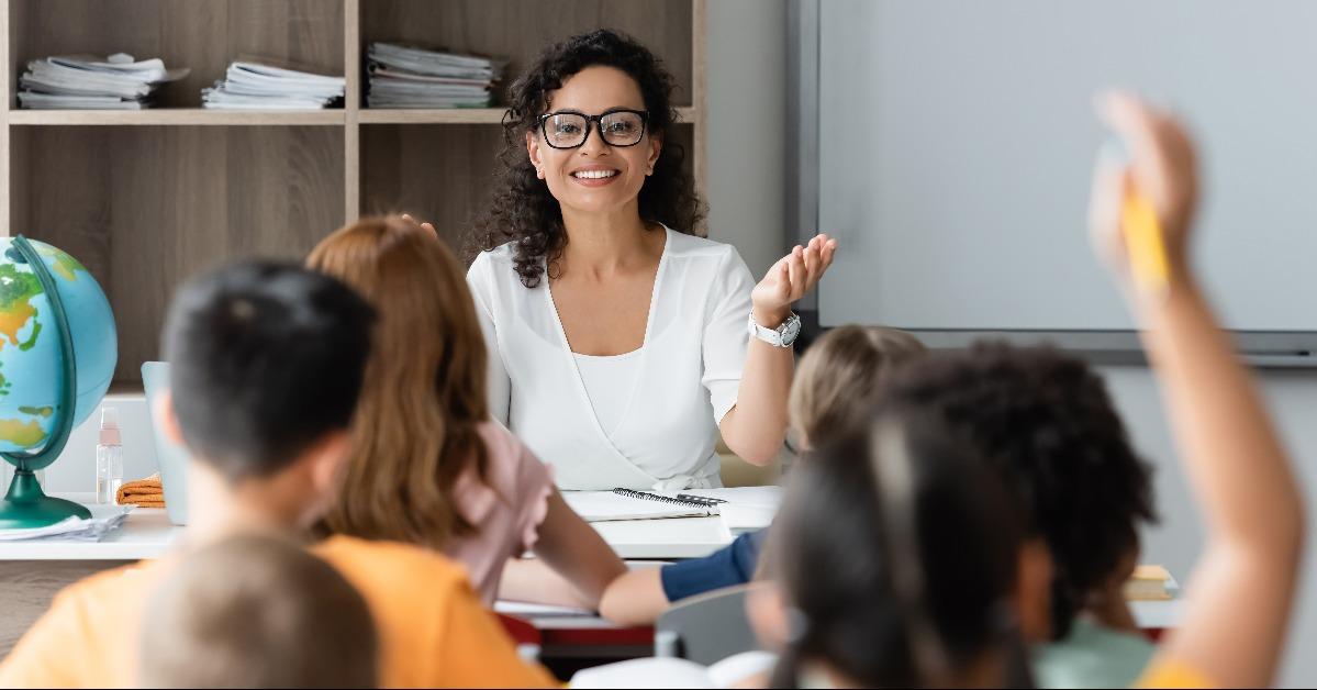  teacher pointing at blurred girl raising hand in classroom