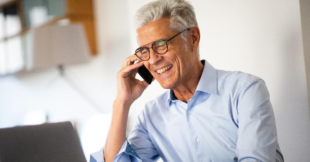 smiling businessman talking with phone while looking at laptop