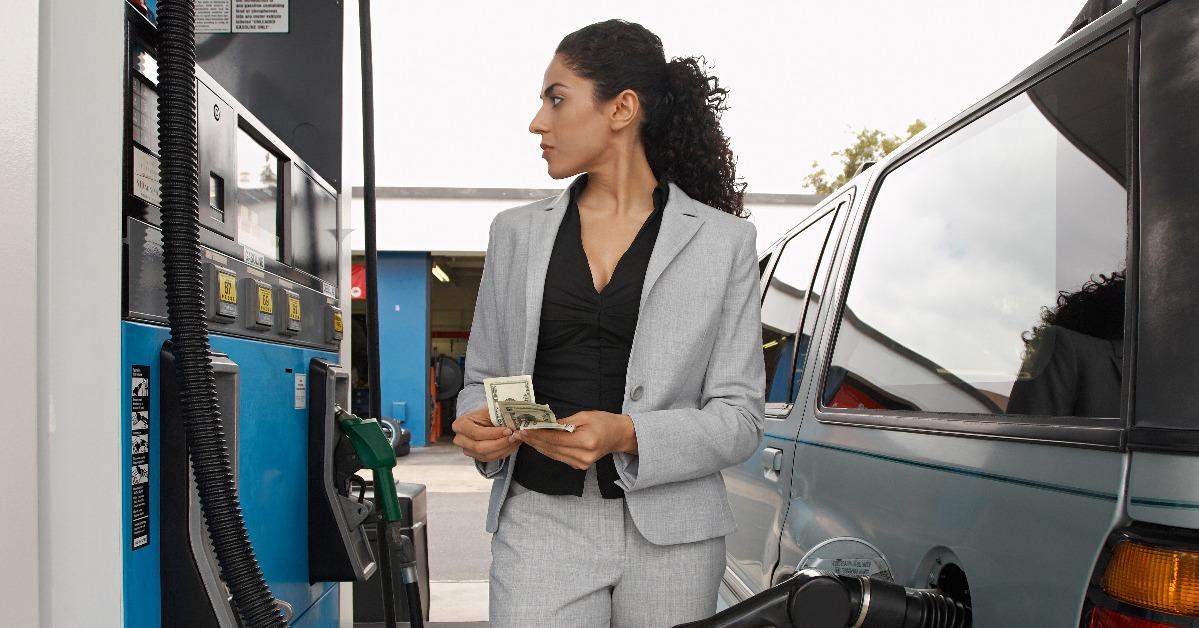 businesswoman counting money while looking on the meter of petrol pump