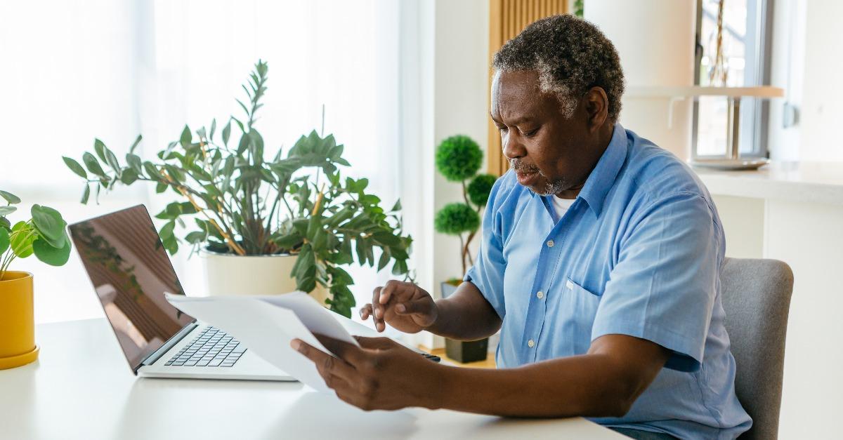 man sitting in his home office with bills in hands and paying it online over laptop