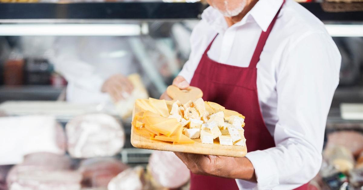 salesman holding cheese on cutting board in shop
