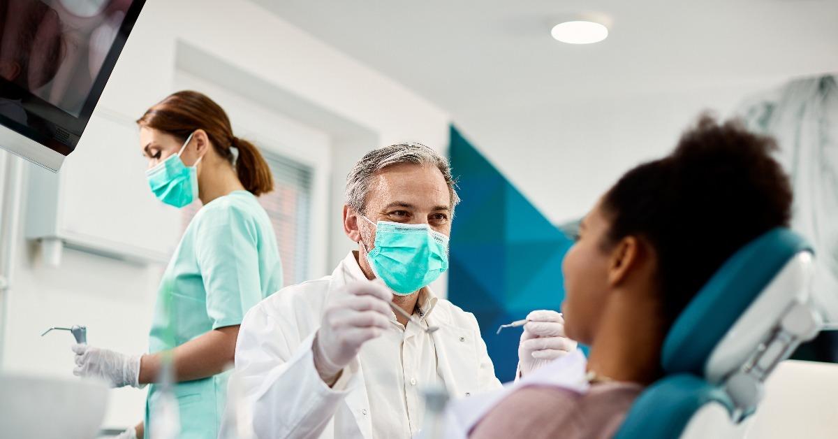 dentist with face mask talking to a female patient during dental procedure 
