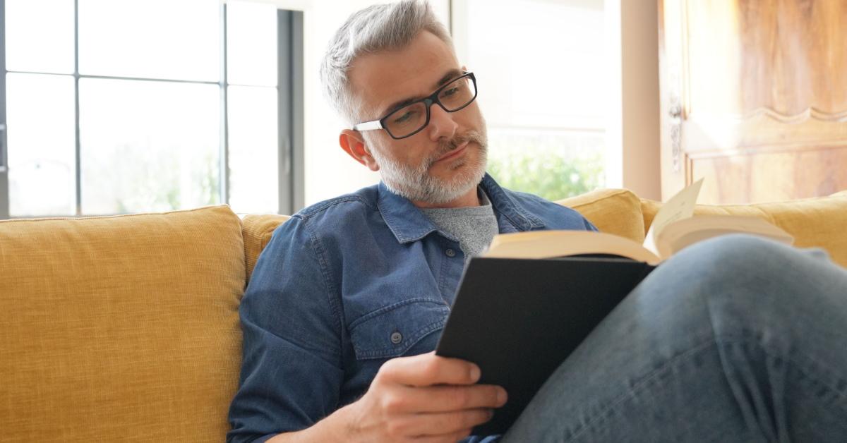 man in white beard reading a book on couch
