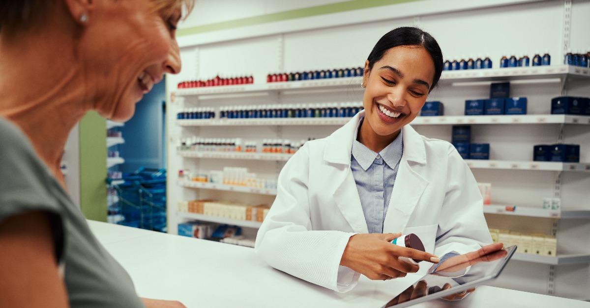 woman wearing lab coat working in pharmacy showing screen to female customer