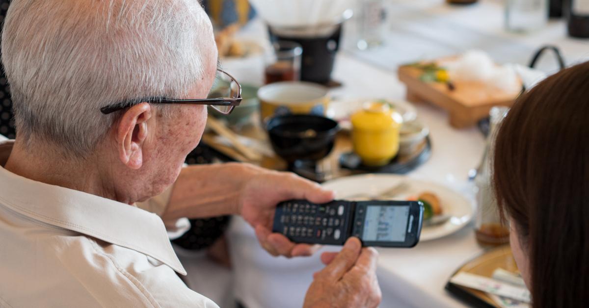 elderly Asian man struggling to use an old fashioned flip phone