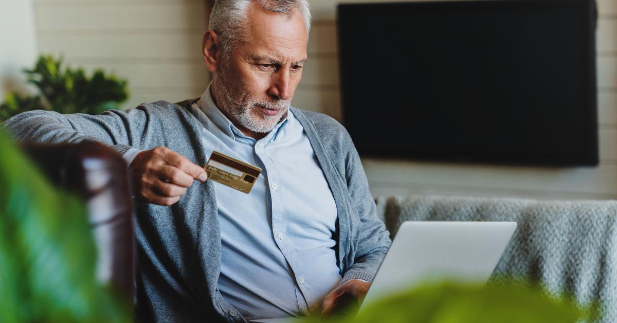 senior man sitting on sofa with laptop and using credit card