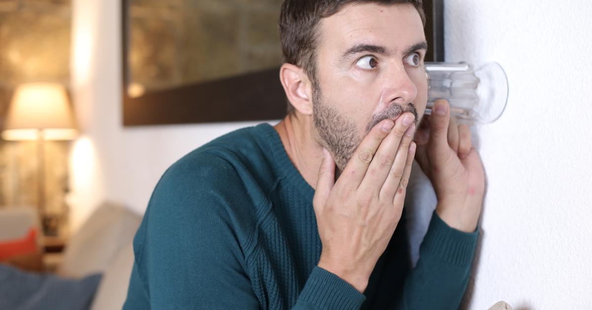man using glass to gossip through wall
