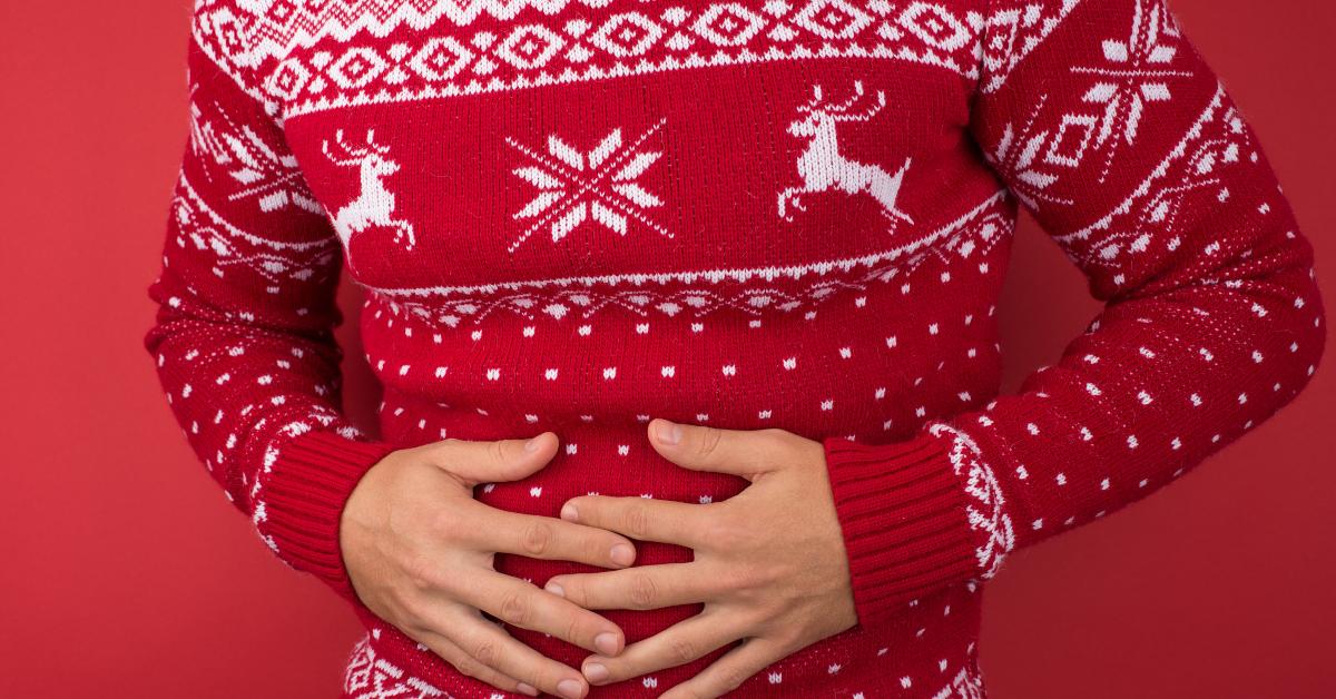 man in red and white christmas sweater holding his hurting stomach
