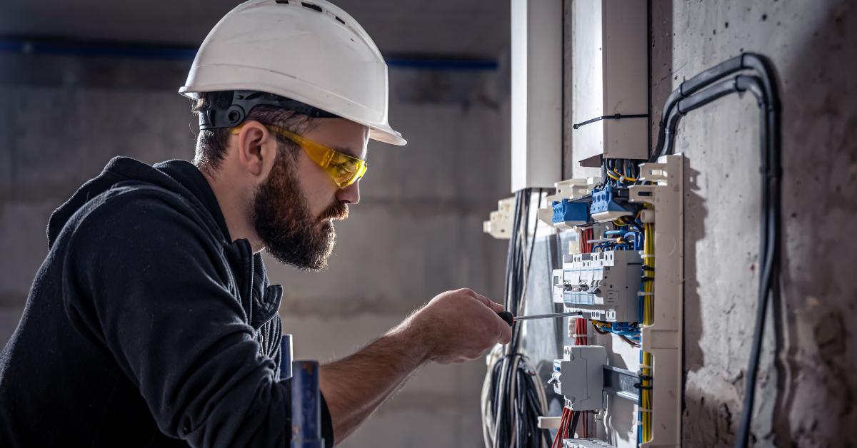 male electrician works in a switchboard with an electrical connecting cable