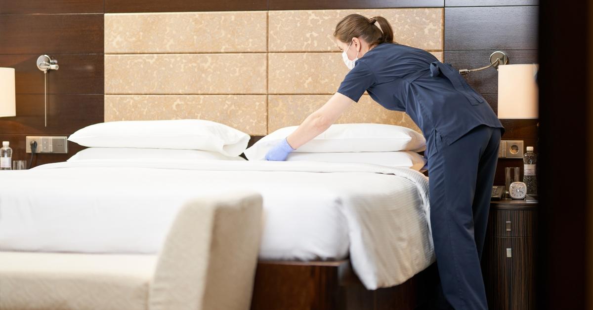 housemaid standing near bed while cleaning the room in hotel