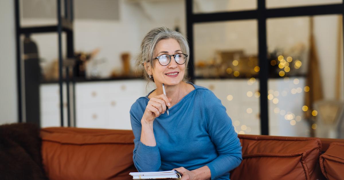senior woman in glasses thinking and writes in a diary home