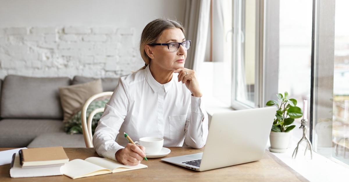 mature female writer sitting at desk at home placing chin on her hands