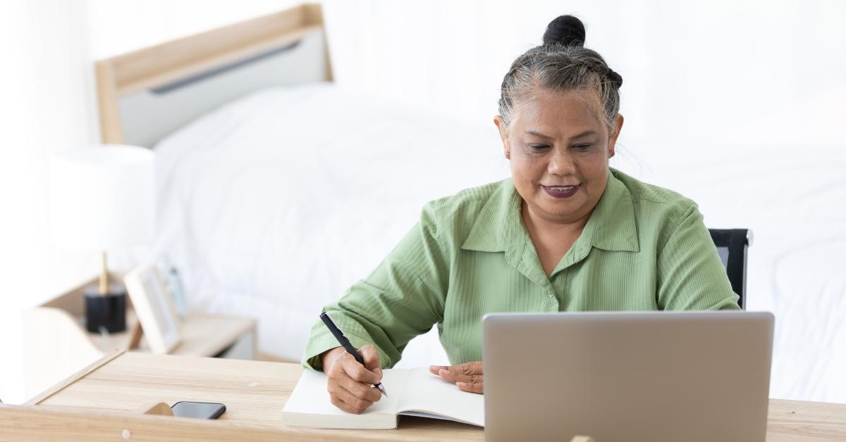 senior woman writing in notebook and using laptop